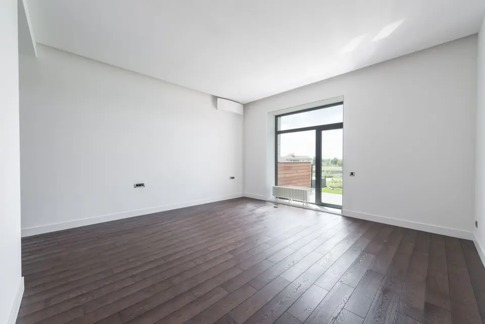 Empty room after renovation: white walls, new wooden floor and a glazed door.