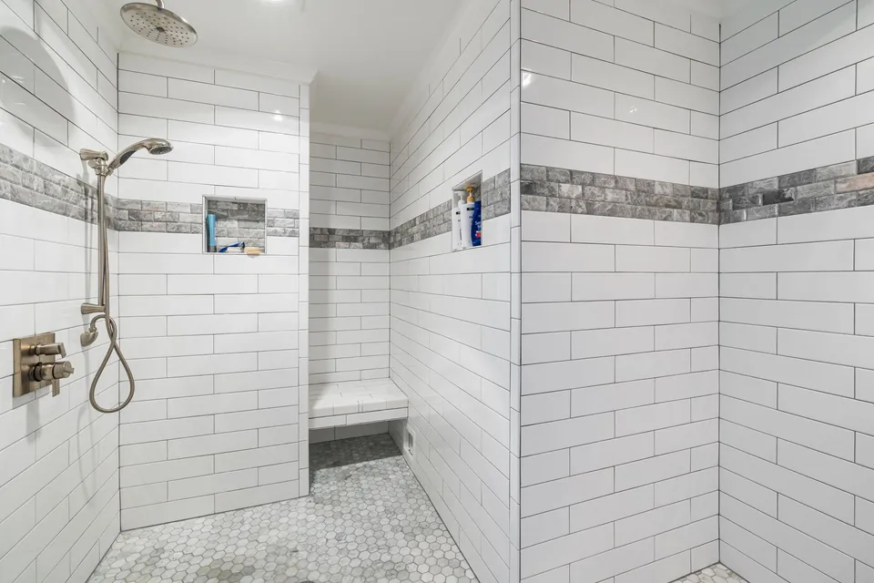 Walk-in shower with white tiles, a bench and a wall niche.