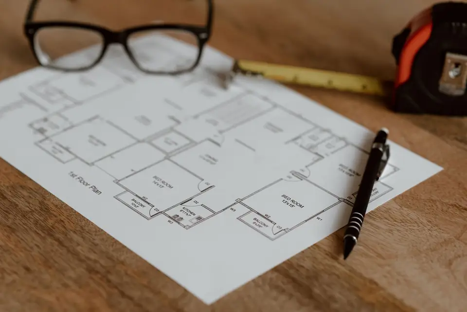 House plan with a ruler, pencil and tape measure on a table.