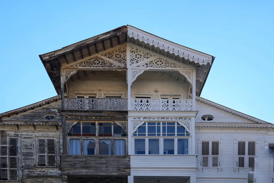 Half-restored ornate timber facade: weathered wood on the left, repainted white on the right.