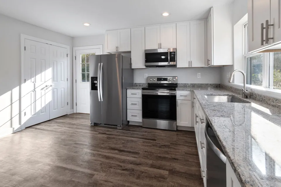 Renovated kitchen: white cabinets, granite worktop, stainless-steel appliances and wooden floor.