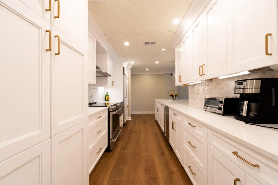 Galley kitchen with white cabinet fronts, brass handles and a wooden floor.