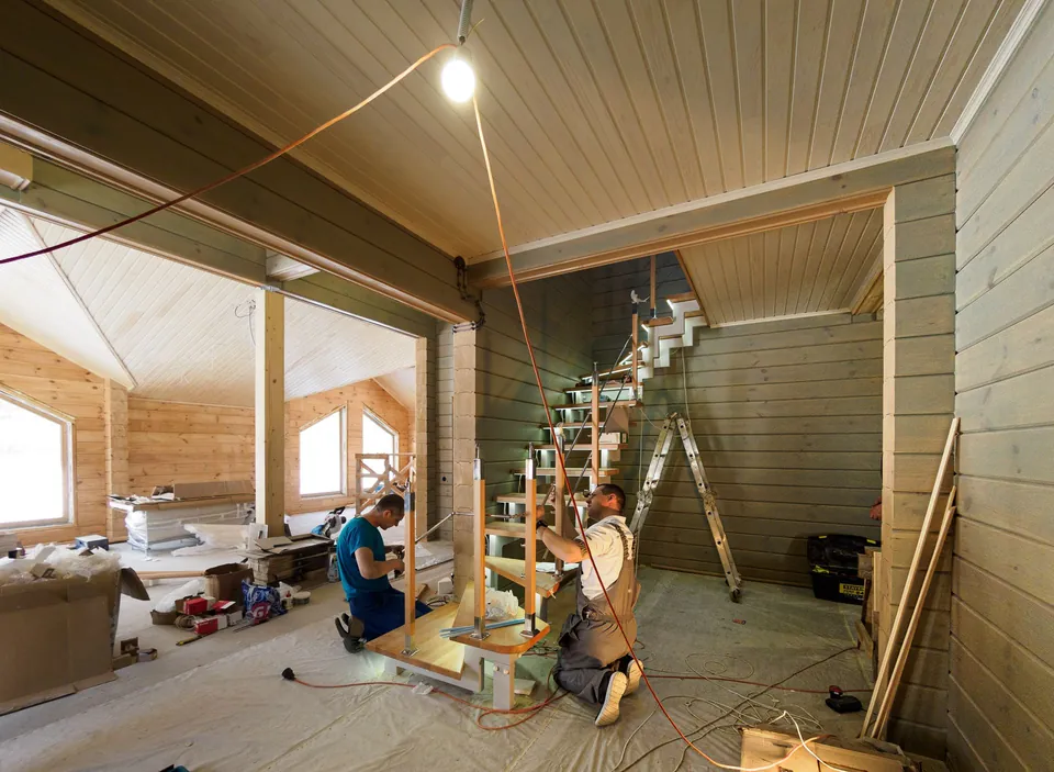 Two carpenters installing a staircase in a timber-framed house.