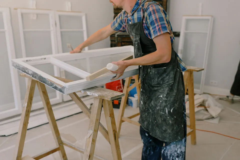 Craftsman in an apron sanding a window frame on trestles.