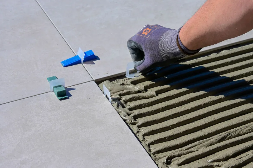 Gloved hand setting a large tile on adhesive, with levelling clips.