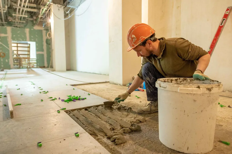 Tiler in a hard hat spreading adhesive before laying floor tiles.