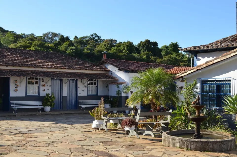 Paved courtyard with a fountain, plants and white houses with blue shutters.