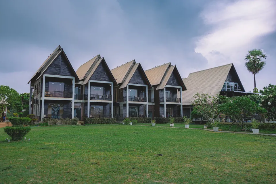 Houses with triangular gables beside a lawn under a cloudy sky.