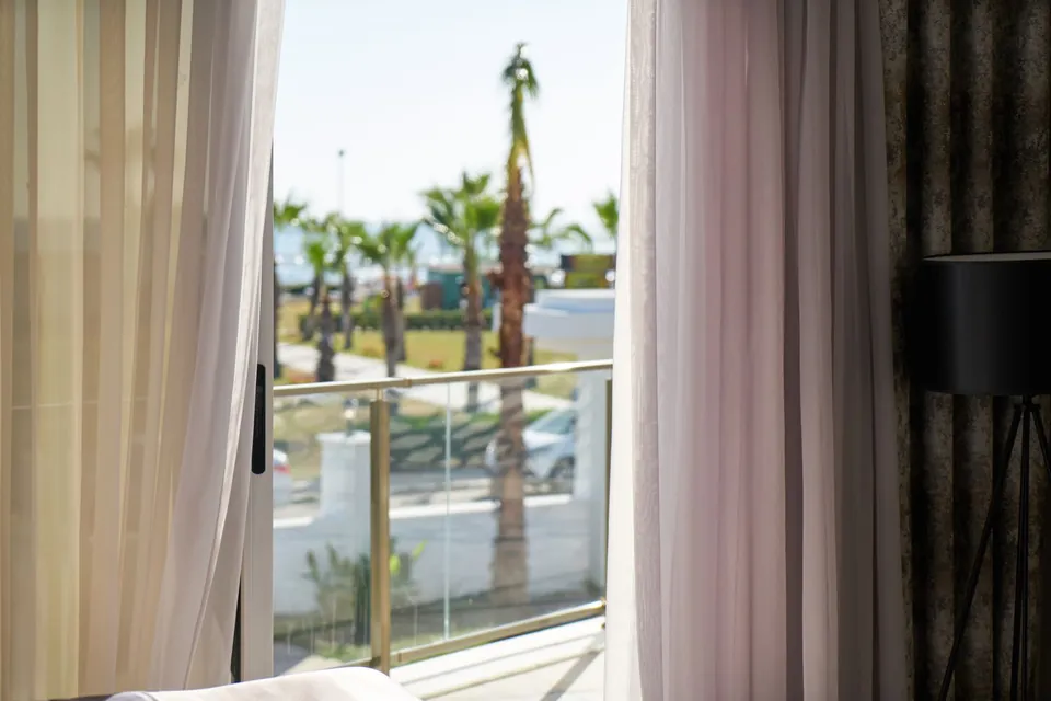 Bedroom with white sheer curtains opening onto a balcony and palm trees.
