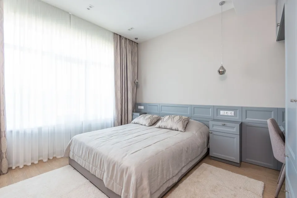 Light bedroom in grey tones with a large bed and sheer curtains.