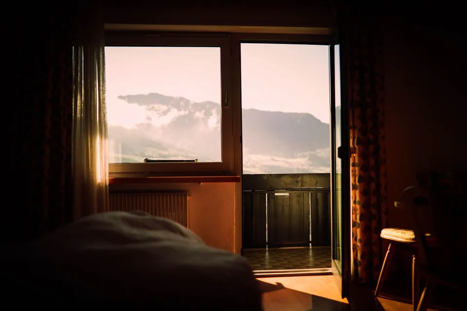 Dim bedroom with a window open onto the mountains at sunset.