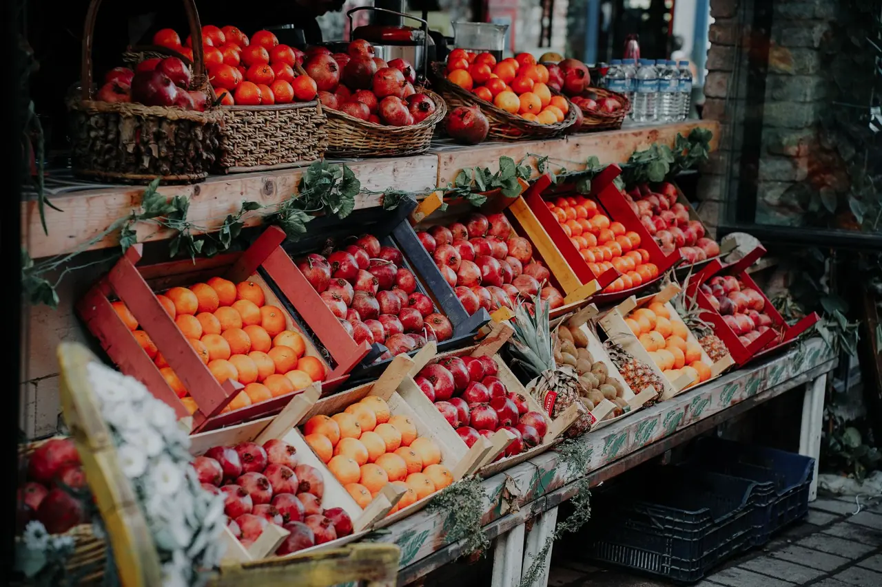 Fruit stall with colourful crates and baskets of tomatoes above.