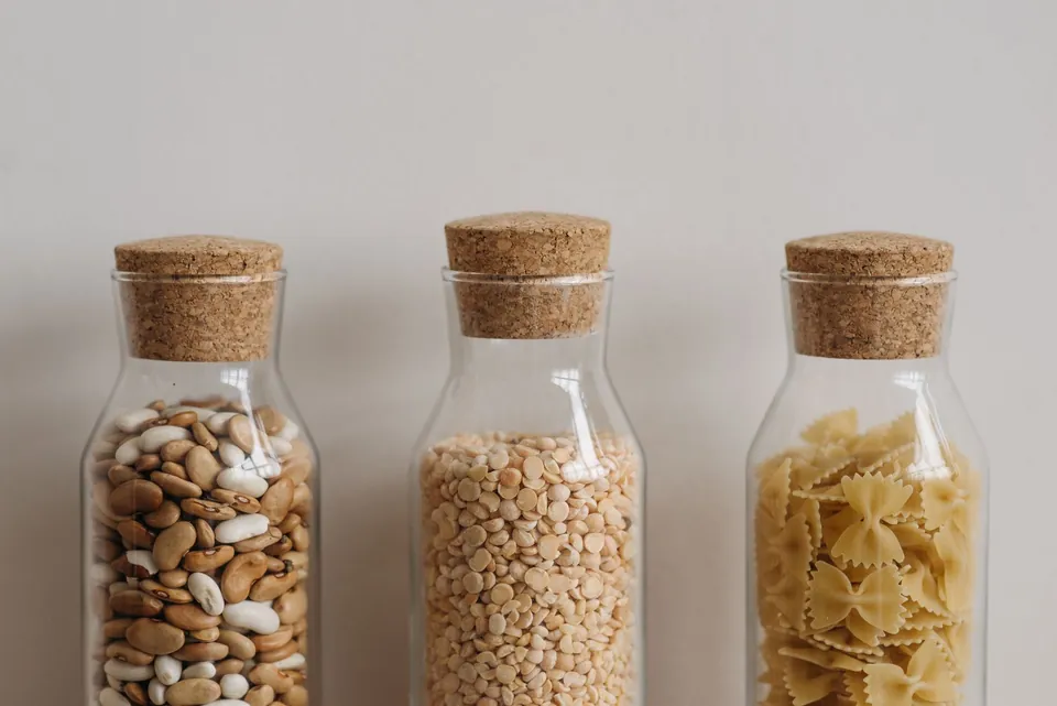 Cork-stoppered glass jars of beans, split peas and bow-tie pasta.