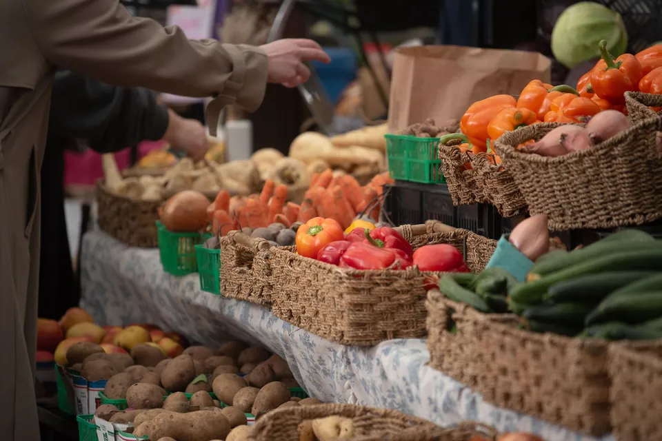 Woven baskets of peppers, tomatoes and potatoes on a market stall.