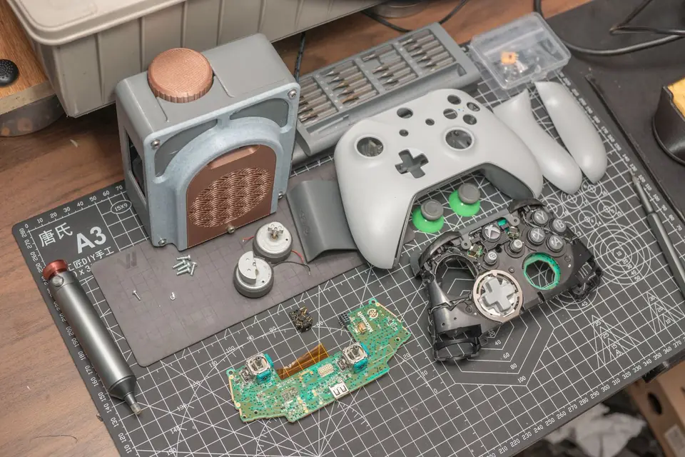 Disassembled game controller, board and buttons laid out on a cutting mat next to tools.