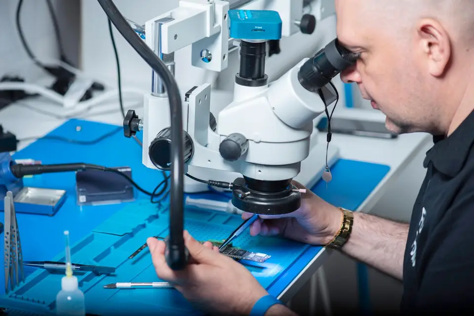 Technician examining a circuit board under a microscope.