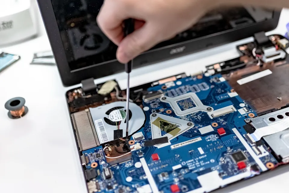 Hand unscrewing a part on the motherboard of an opened laptop.