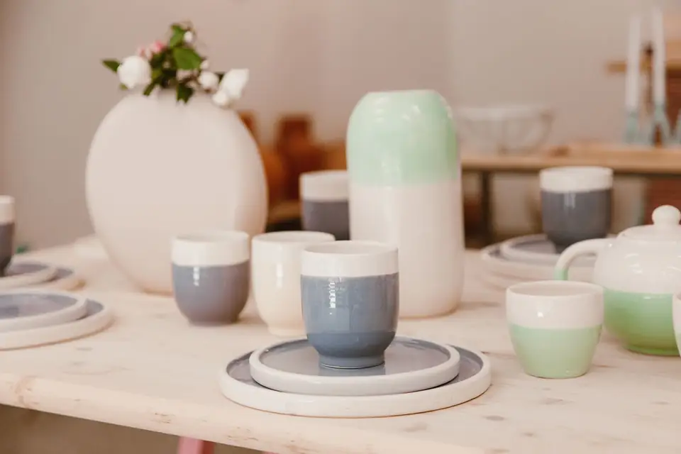 Ceramic tableware, cups and a vase set on a wooden table.
