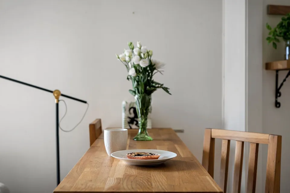 Solid wood table with a bouquet of white roses, a wooden chair and a black floor lamp.