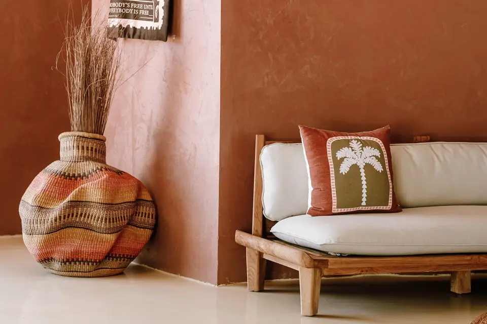 Living room with terracotta walls, a wooden daybed and a woven vase.