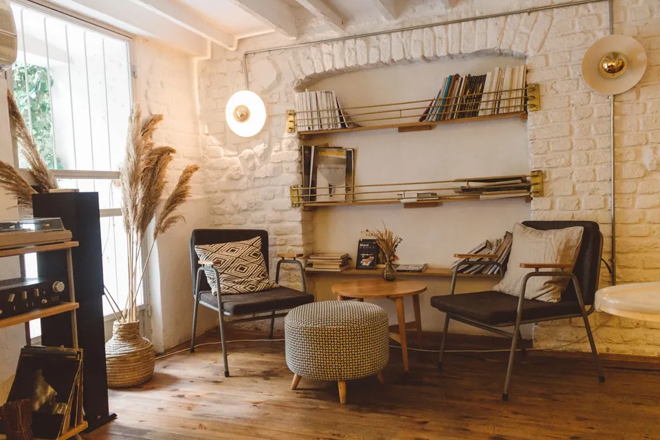 Warm living room: white brick wall, brass shelves, armchairs and a woven pouf.