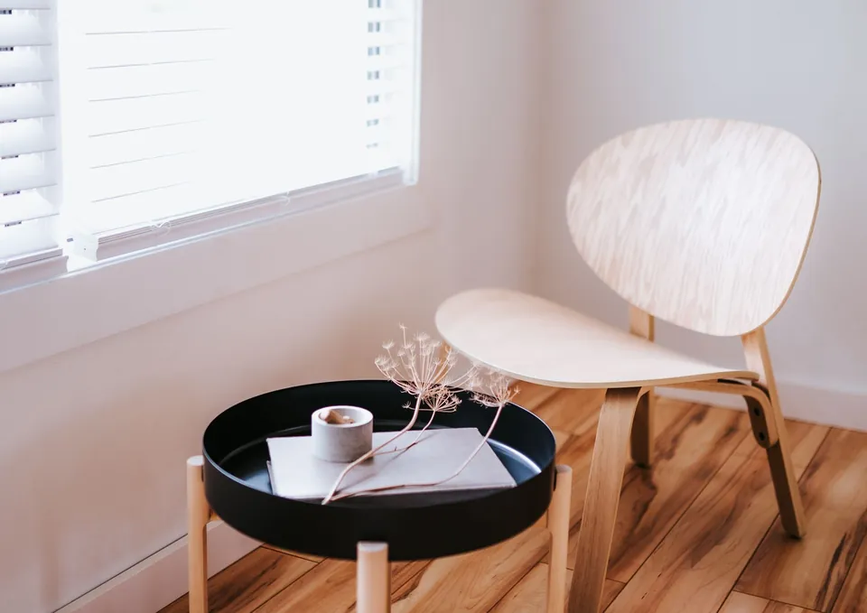 Light wood lounge chair and black side table by a window, understated decor.