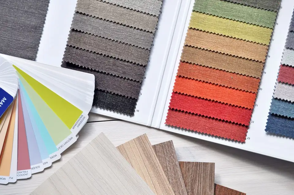 Colourful fabric swatch books, a colour fan and wood samples on a table.