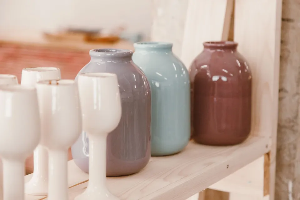 Pastel ceramic vases and white cups lined up on a wooden shelf.