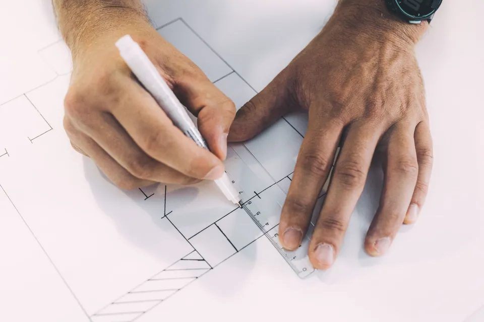 Hands drawing a floor plan with a marker along a ruler.