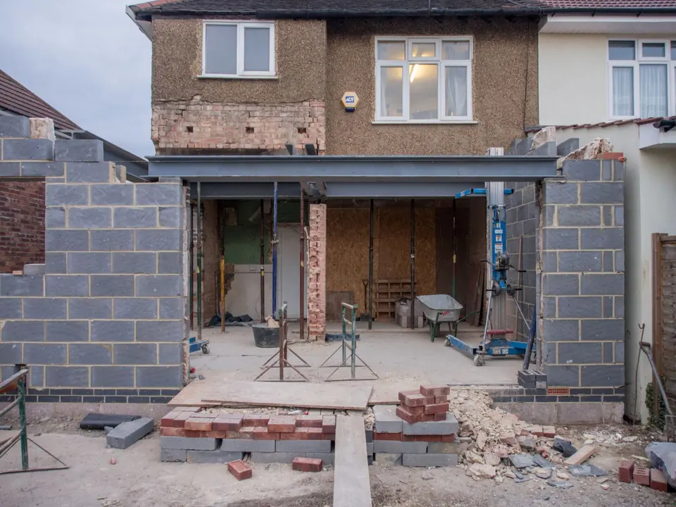 Extension under construction at the back of a brick house, block walls and a steel beam.