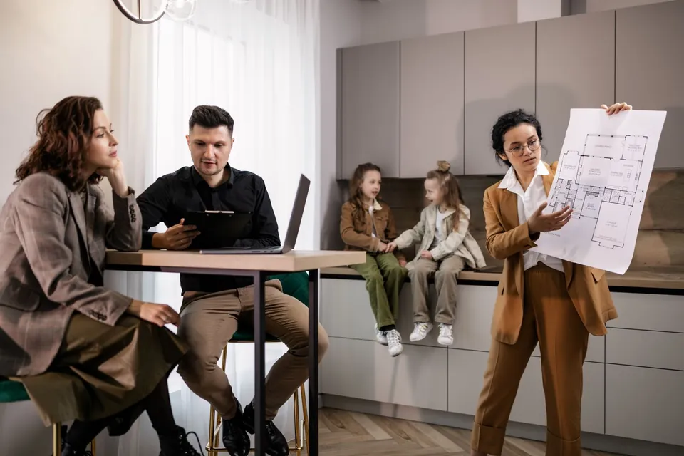 Architect showing a floor plan to a family gathered in their kitchen.