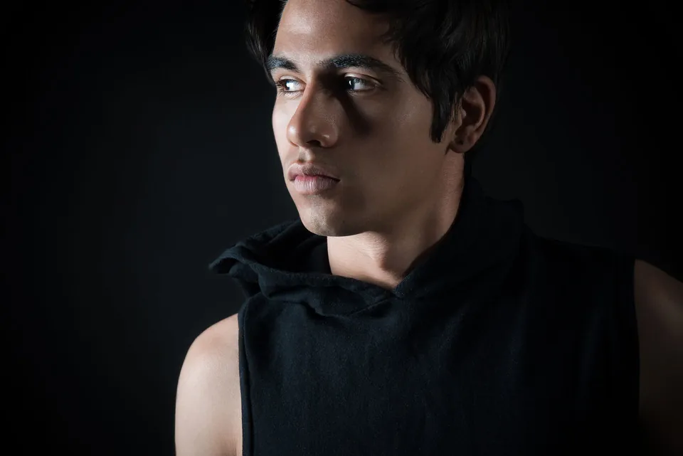 Low-key portrait of a young man in a black top against a dark background.