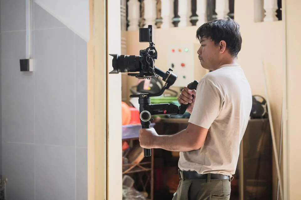 Videographer holding a camera on a stabiliser at the entrance of a house.