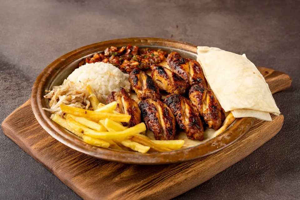 Grilled chicken served with rice, fries and flatbread on a wooden board.