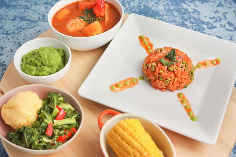 Dishes served together: jollof rice, vegetables, corn and stew.
