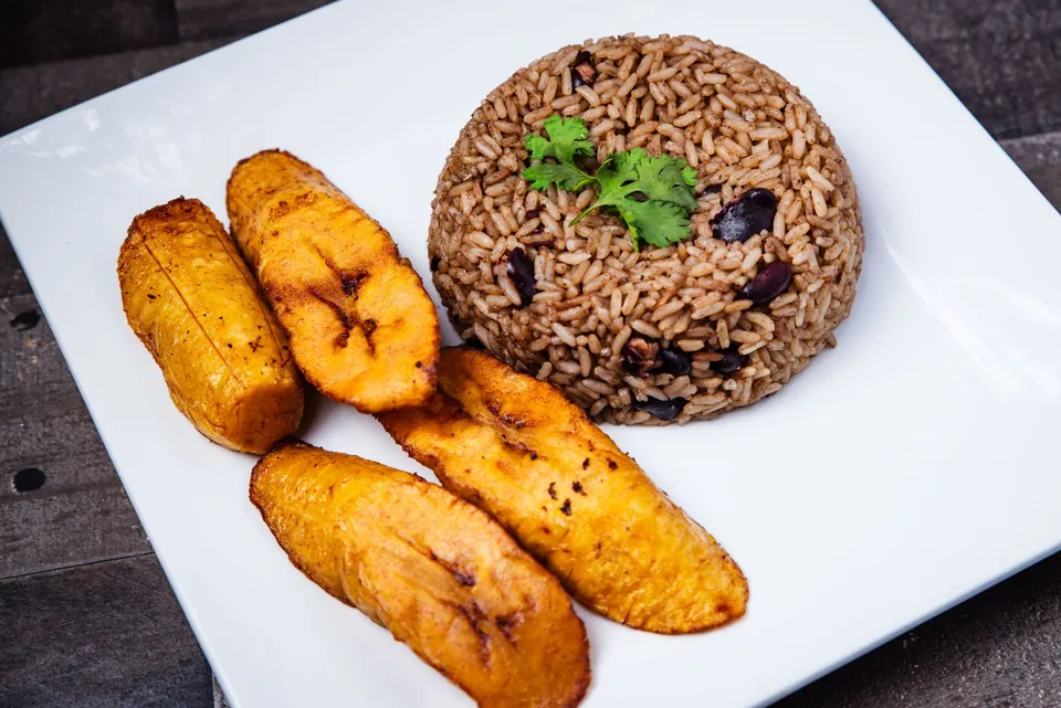 Fried plantains and rice with red beans on a white plate.