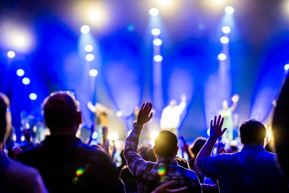 Audience seen from behind in front of a stage lit by blue spotlights.