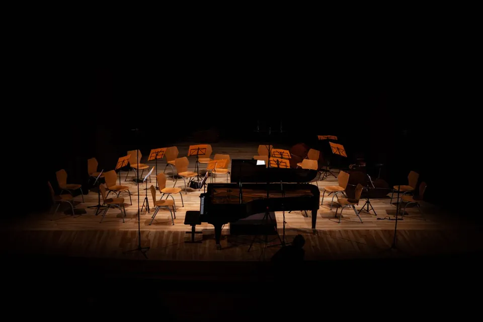 Grand piano and music stands on a stage in near darkness.