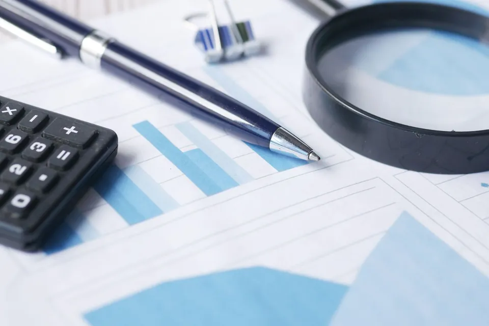 Printed blue charts with a pen, calculator, and magnifying glass on a table.