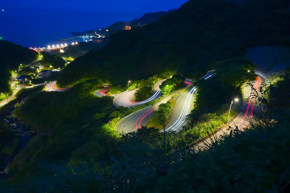 Winding mountain road at night, drawn by light trails.