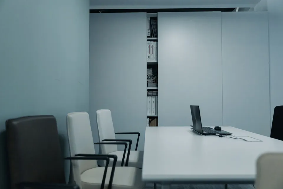 Minimal meeting room: white table, armchairs, and a laptop.