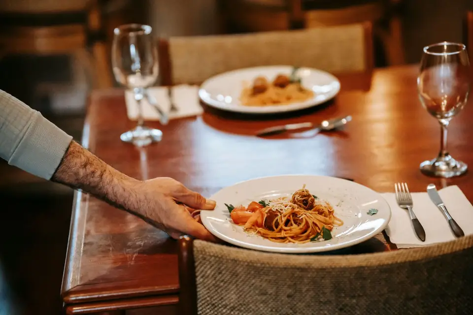 Waiter setting down a plate of pasta on a laid table.